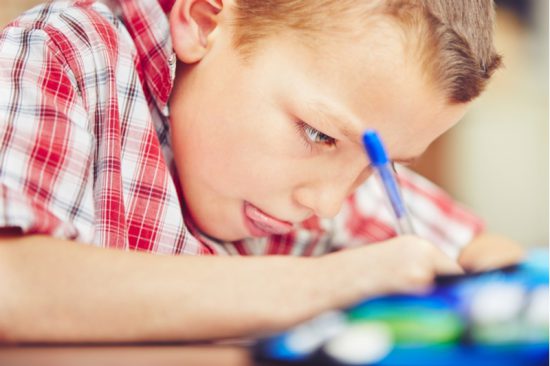 Little boy writing, concentrating hard, head close to paper