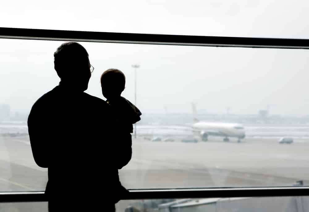 Father holds small child, observation window, airport, metaphor for online safety journey, guided by "The Hitchhiker's Guide to the Galaxy."