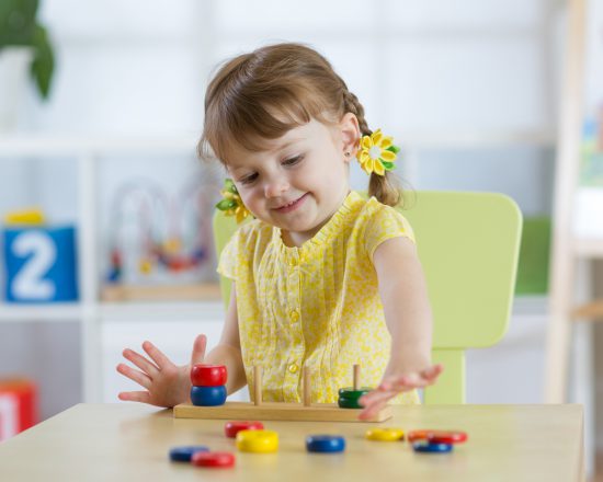 Smiling girl plays with Montessori materials in kindergarten classroom