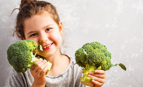 Girl holding broccoli spears illustrates nutrient dense diet