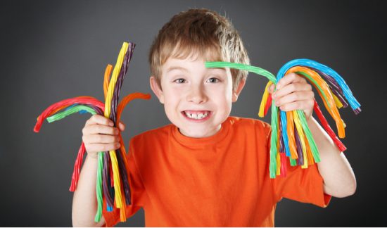 child hyped up on sugar holds colorful licorice sticks (sugar harms metabolism)