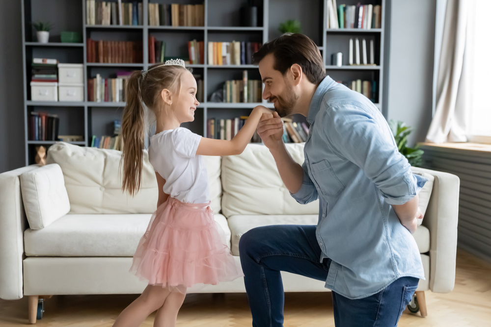 father kneels, kisses hand of daughter dressed like princess, modeling good manners