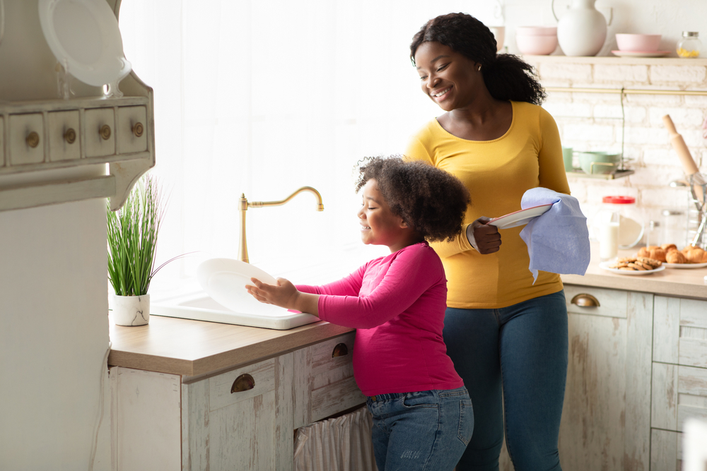 smiling child washes plate next to smiling woman