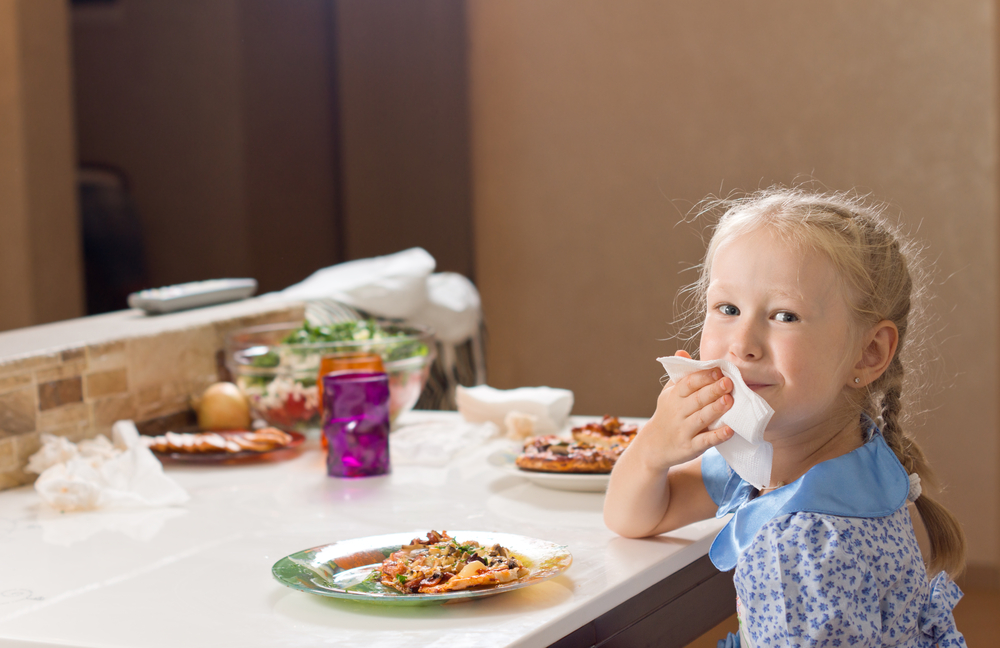 girl blots mouth with napkin while eating at table