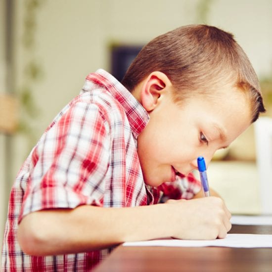 A boy with cowlick and plaid shirt, bent earnestly over his homework