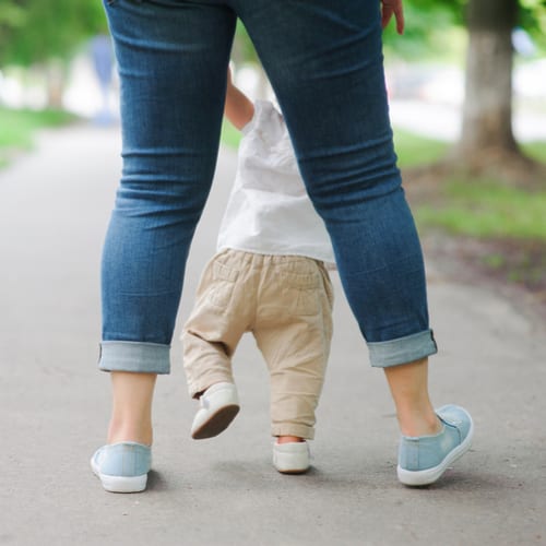 Baby walking holding onto Mommy's hands, seen from behind