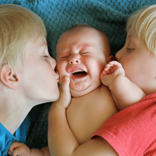 Two blond boys offer close physical contact to the infant lying between them on a bed