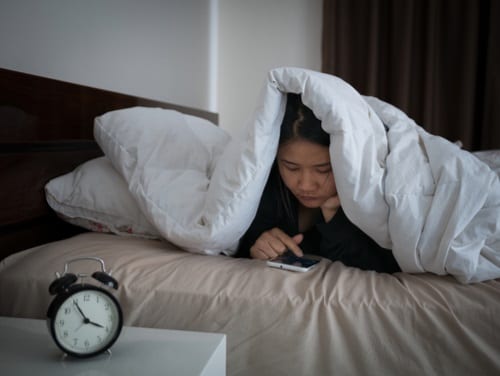 Asian teen texting on her smartphone under the covers