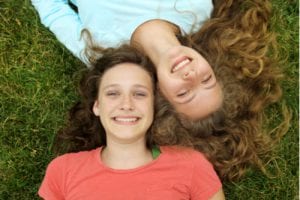 Two young girls lying on the grass in opposite directions, smiling best friends