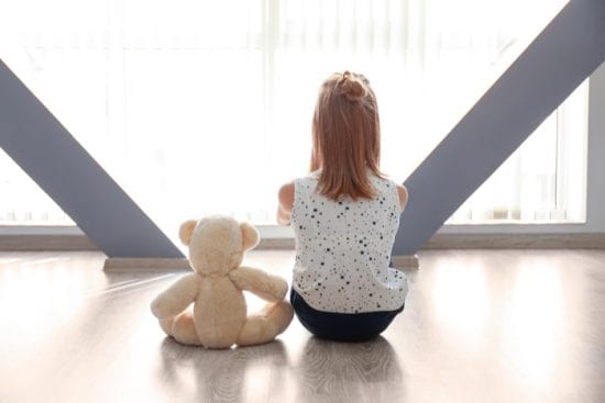 Autism social difficulties illustrated by girl sitting next to teddy, their backs to the camera