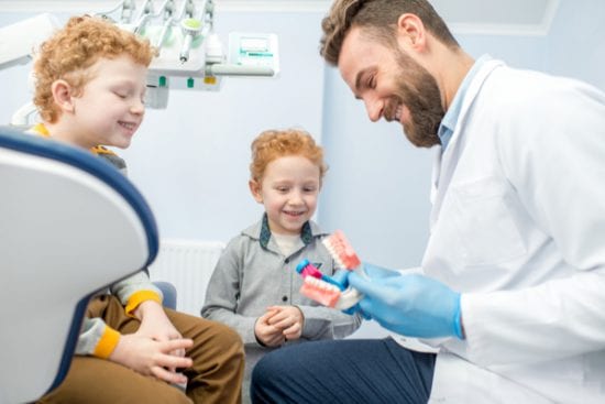 Red-headed brothers get a lesson in tooth brushing from bearded dentist