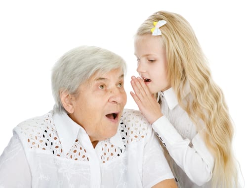 Child whispers in the ear of shocked seated elderly woman