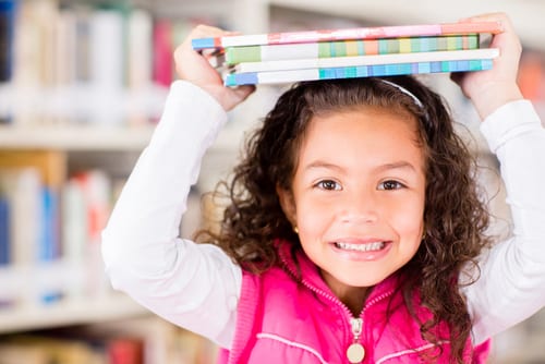 little girl enjoys summer library fun with books on head