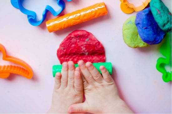 child rolls out homemade playdough with miniature plastic rolling pin