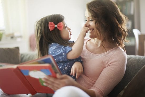 Little Girl touches smiling mothers nose as mom reads storybook