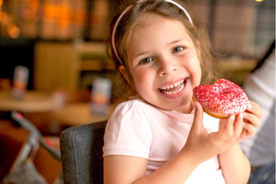 Smiling girl holds donut to illustrate risk of childhood obesity leading to type 2 diabetes