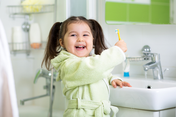 Smiling pigtailed girl holds up toothbrush