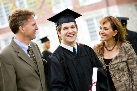 Smiling male graduate surrounded by proud parents, illustrative of Age-based graduation or graduating "on time."