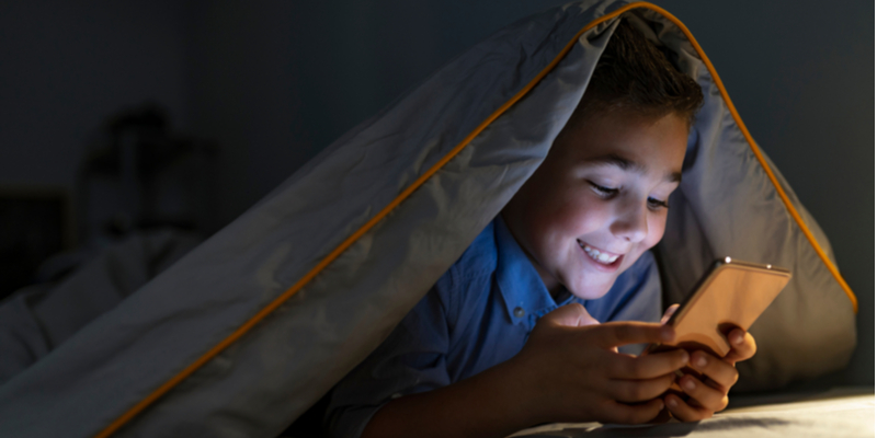 child with smartphone texting under covers at night