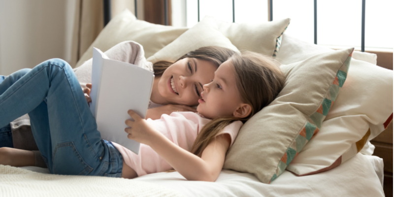 smiling calm mother and daughter reading together in bed