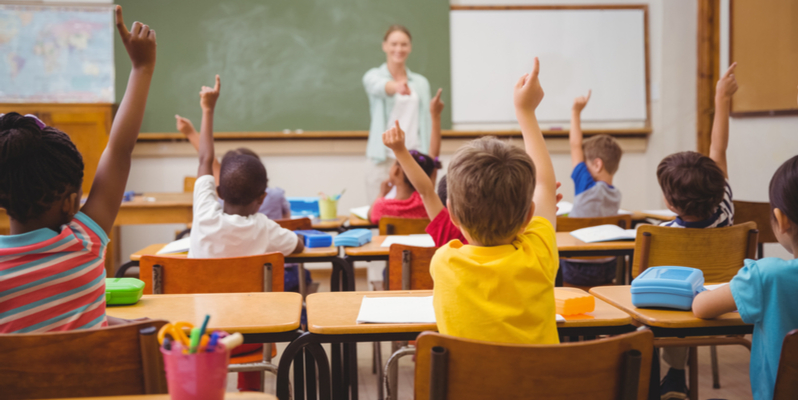 Smiling teacher kids with raised hands in classroom