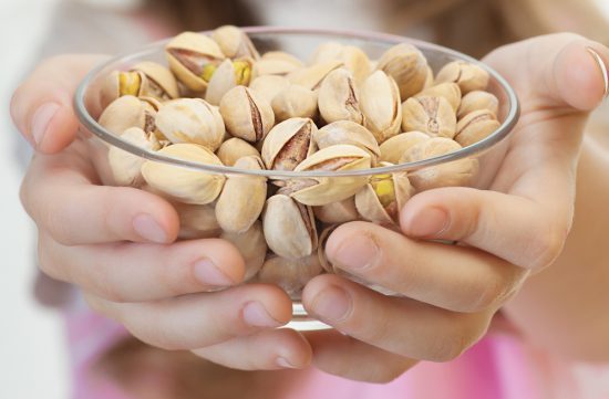 Child's hands holding bowl of pistachio nuts, to illustrate Do You Have to Soak Nuts and Seeds? Apparently Not