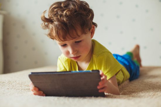 little boy playing with digital tablet lying on a bed