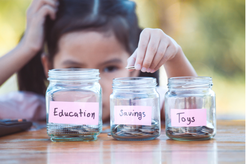 Girl puts allowance into jars labeled education savings toys