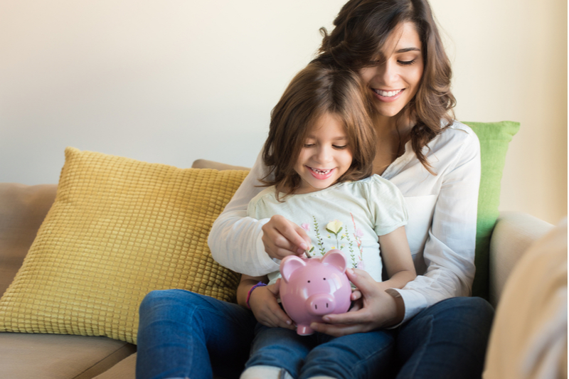 Mom helps little girl put coins in piggy bank