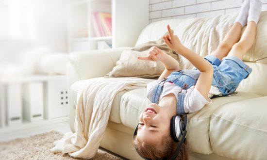 Little girl wearing earphones hanging off couch during "Coronacation" Covid-19 vacation