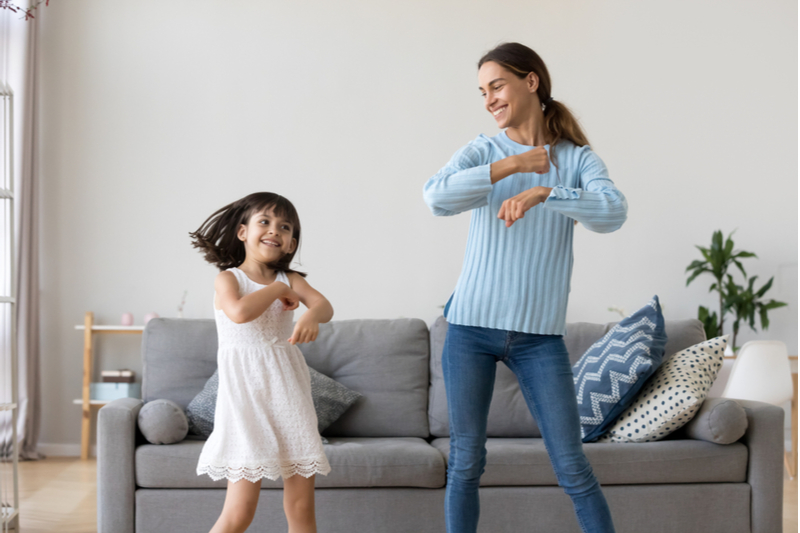 cheerful mother little daughter dancing in living room