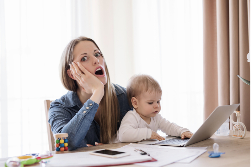 mother in horror working from home with baby taking over laptop keyboard 