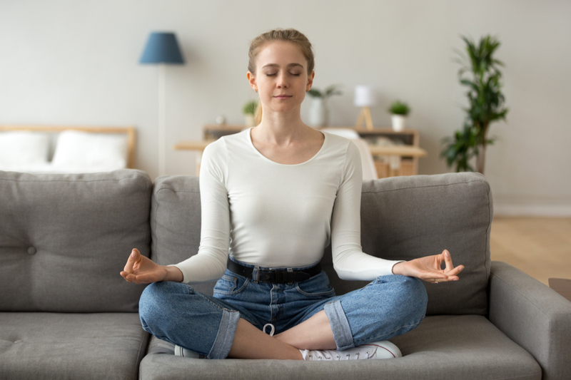 serene mom meditating in lotus position on sofa