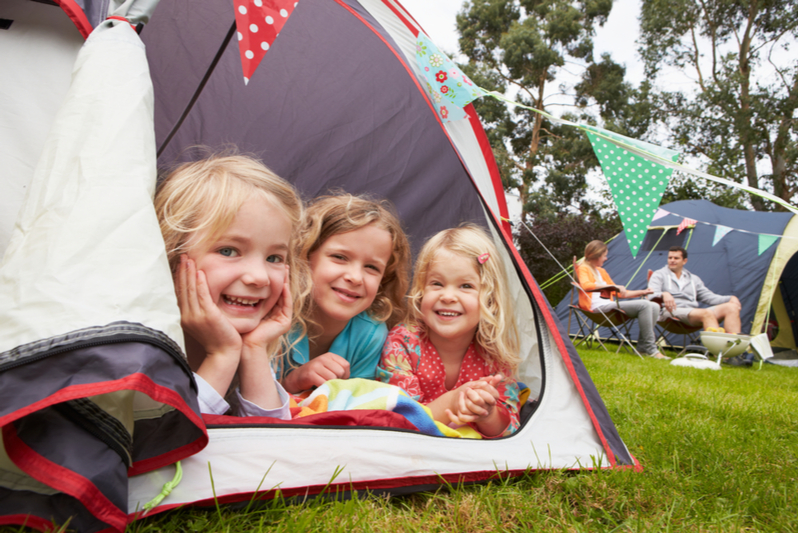 Family camping. Smiling girls peek out of tent