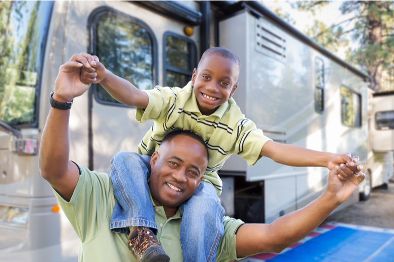 African American father with son on shoulders in front of RV