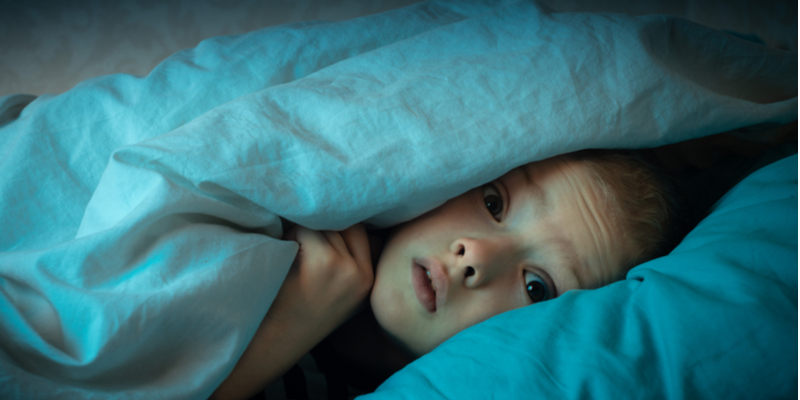 frightened child having nightmares peeks out from under the covers