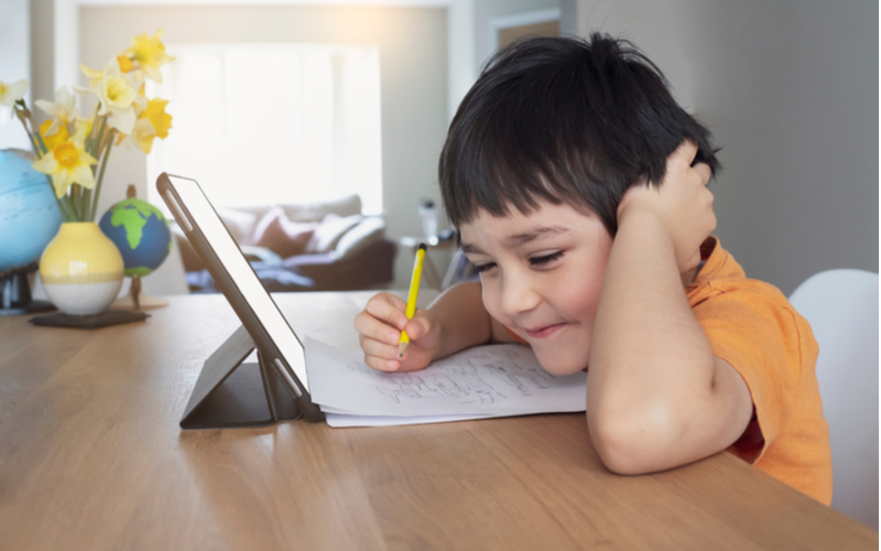 The little boy happily taking notes while using tablet illustrates educational term blended learning