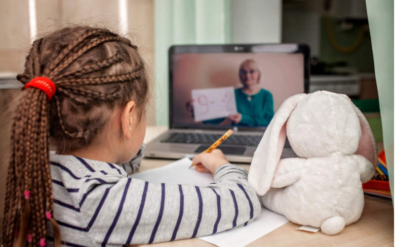 Little girl takes online class with teacher illustrating the educational term "synchronous learning"