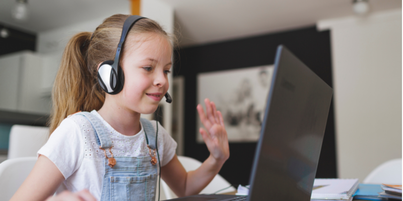 pretty young girl waves to friend on screen while wearing headset