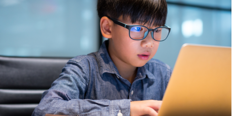 studious preteen asian boy blue light reflected in glasses from screen time