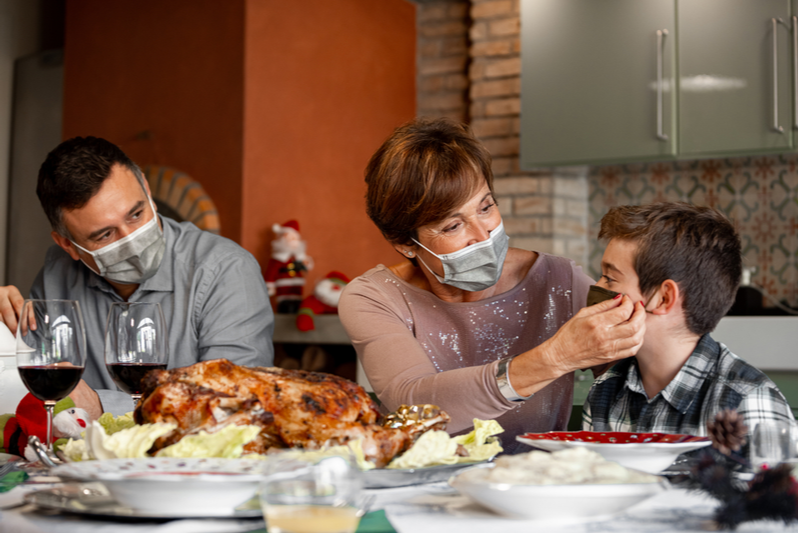 holiday visits 2020: parents adjust mask on son at festive meal