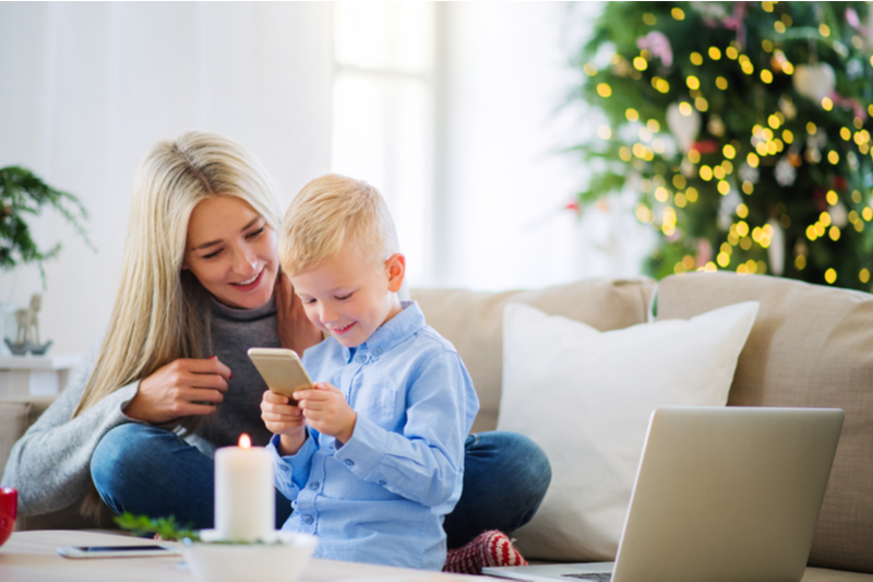 Smiling Mom and little blond boy watch phone video 