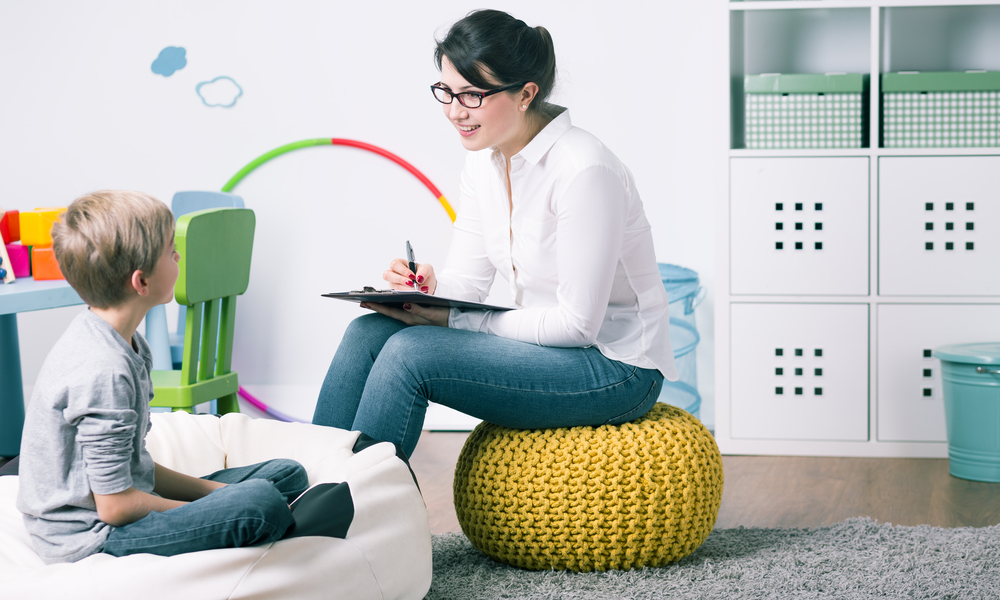 Smiling therapist sits on pouf, works with young boy