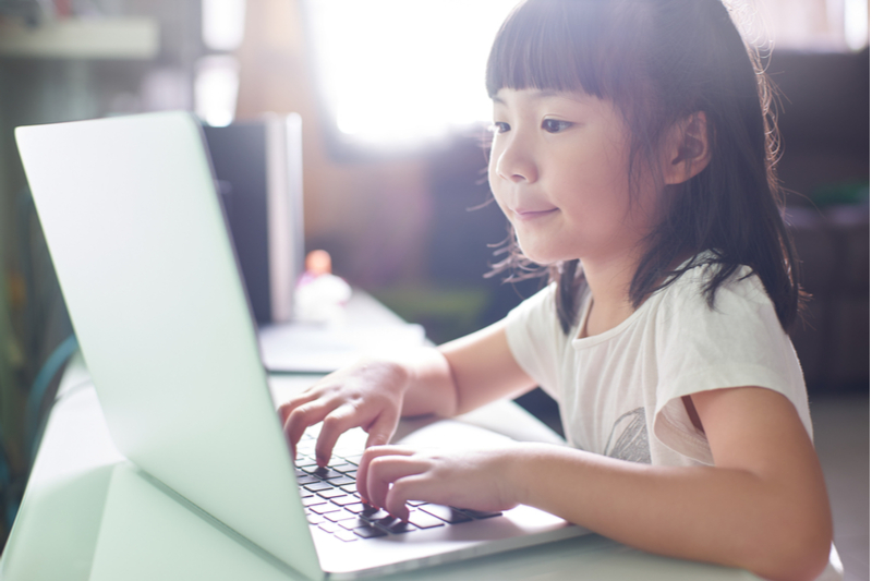 Learning to problem solve Smiling Asian girl works on schoolwork alone at laptop