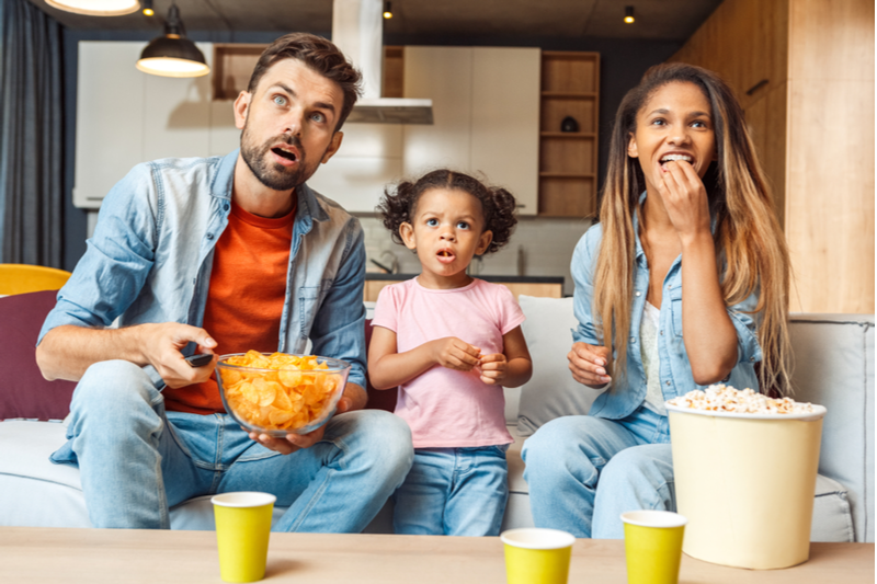 biracial family watches tv while snacking