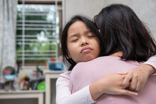 Grieving Asian girl is hugged by female social worker