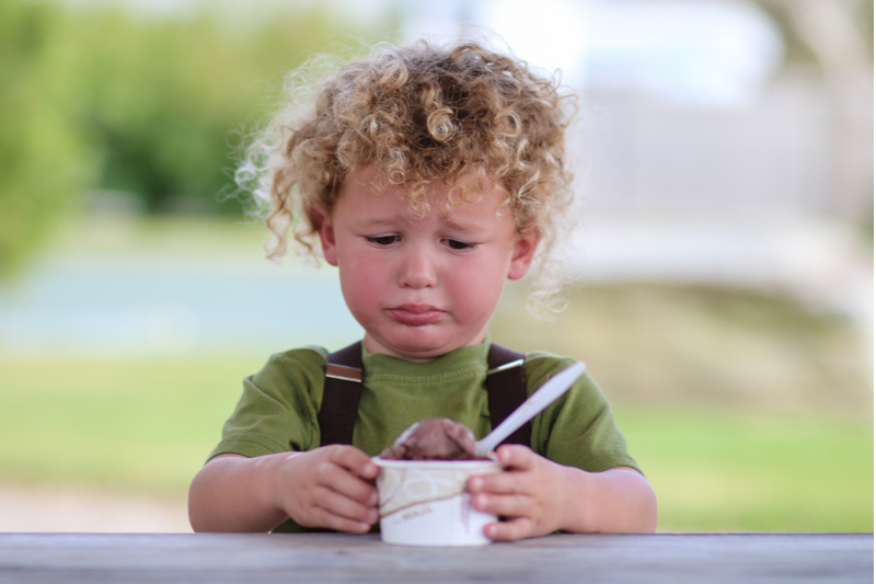 sad child holds cup of ice cream