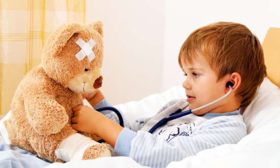 Sick at home boy plays doctor with teddy bear patient