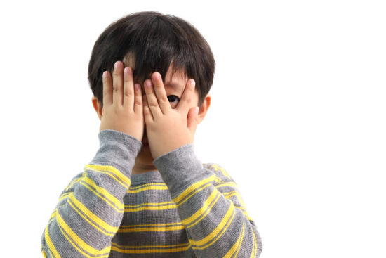 Asian boy peeks through fingers as example of shyness in children