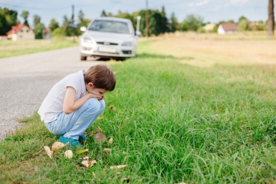 Child kneels side of road carsickness